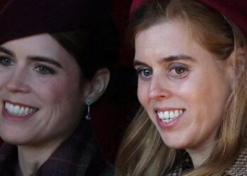 Princesses Eugenie and Beatrice, seen in close-up, smiling and looking off camera - they are both wearing coats and hats