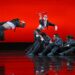 Dancers in suits on a red stage.