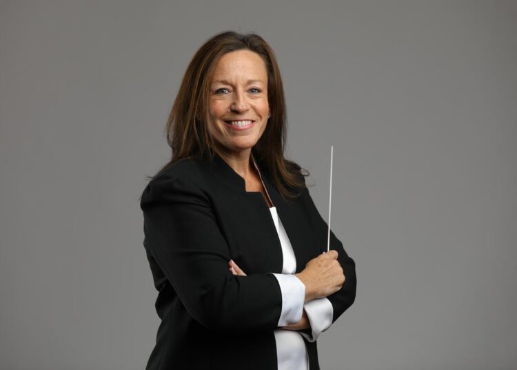 White woman with dark hair, holding a conductor's baton. Paladin Regiment.