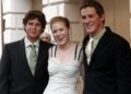 Woman in a white dress stands between two young men in suits