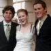 Woman in a white dress stands between two young men in suits
