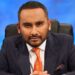 Amol Rajan wearing a blue suit and orange tie, sat on a chair and sat forward looking Ahead.