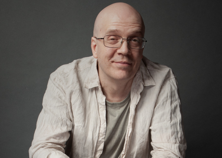 Devin Townsend sitting in a professional studio, looking thoughtful and surrounded by music equipment.