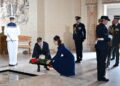 A man and woman lay a wreath on the ground together.