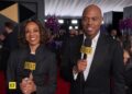 A woman and a man in black clothing holding microphones on a red carpet.