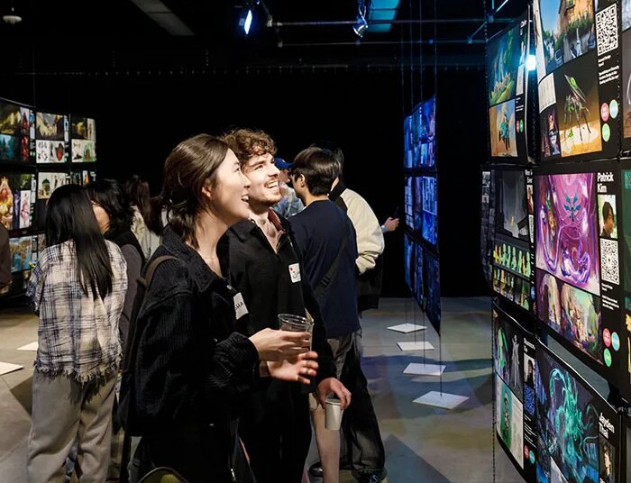 two college-aged adults smile up at backlit art displays down a long dark corridor lit by commercial art