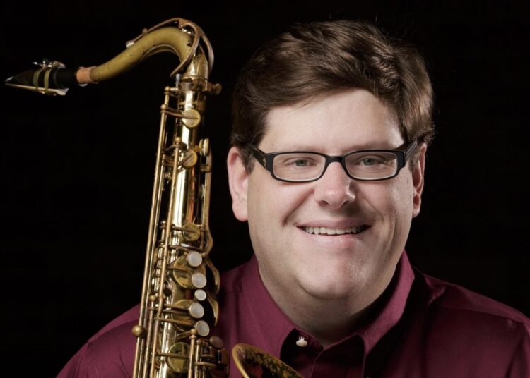 A white man wearing glasses is holding a saxophone. Matt Olson