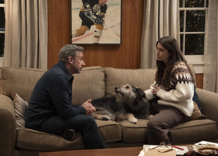 A man and a woman sit on a couch with a dog between them.