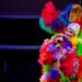 An Elton John tribute performer on stage covered in colorful feathers and big glasses