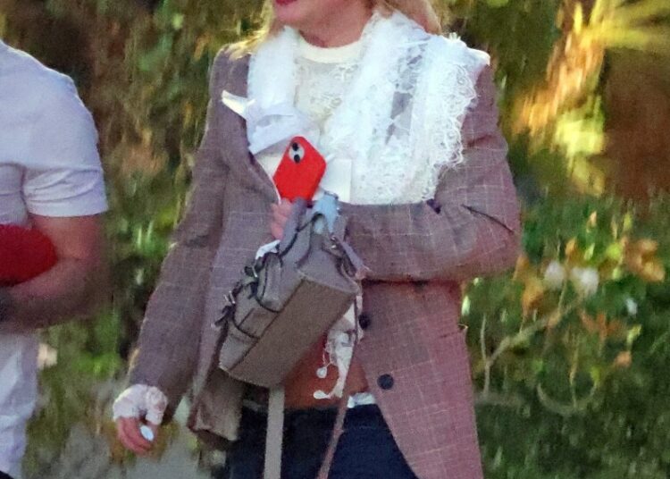 Britney Spears wearing sunglasses, a brown blazer, a white lace top, and blue jeans, walking outdoors.