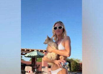 Brittany Snow posing in a white ribbed bikini and mod sunglasses while holding a small dog and a disco ball cup.
