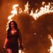 Kacey Musgraves stands on stage in a black dress in front of the shape of a heart on fire