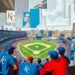 A fractured, multi-perspective painting depicting the Kansas City Royals' baseball stadium and surrounding cityscape broken down into sharp, overlapping geometric planes in vibrant blues, reds, and muted greys, conceptually representing the team's relocation plans.