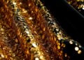 An extreme close-up photograph of shimmering, textured sequins and glittering glass shards, conceptually representing the luxurious materials and finishes found in celebrity homes.