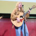 Musician performing on stage with an acoustic guitar.