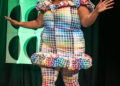Plus-size woman in colorful grid-patterned outfit expressing excitement on stage, related to celebrities people now hate.
