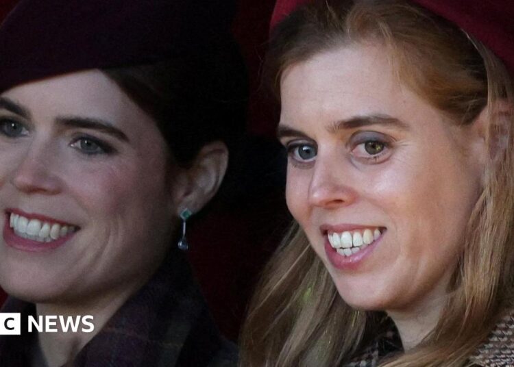 Princesses Eugenie and Beatrice, seen in close-up, smiling and looking off camera - they are both wearing coats and hats