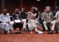 Mary and Frederik sit on chairs watching a man perform a ceremonial dance
