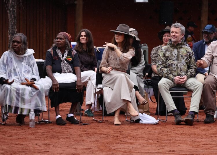 Mary and Frederik sit on chairs watching a man perform a ceremonial dance