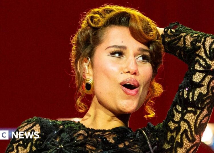 Raye smiles as she performs on stage in a black ballgown
