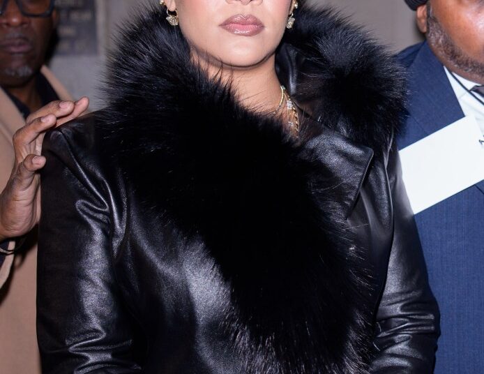 Rihanna in a black leather coat with a fur collar.