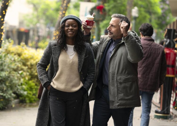 A woman in a beanie, sweater and dark coat smiles and walks next to a man holding a hot cocoa in his raised hand.