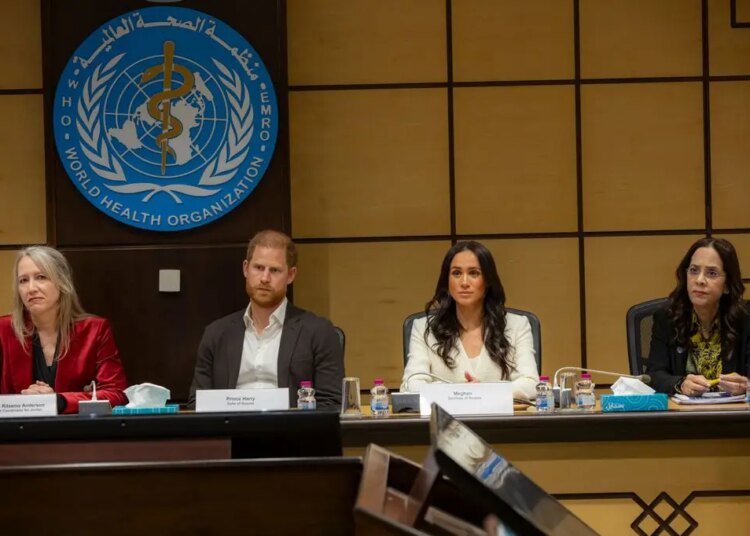 Prince Harry with a stern face sitting at a roundtable