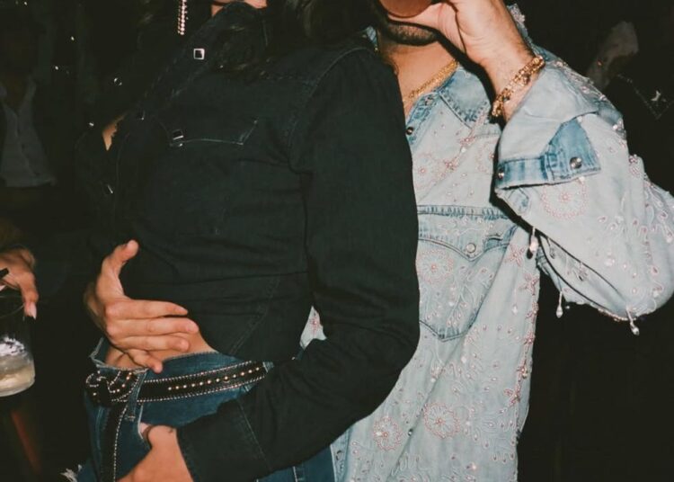 Two people posing together in a social setting, wearing stylish outfits.