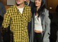 a man in a yellow plaid shirt stands next to a woman in a gray coat and black pants