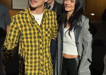 a man in a yellow plaid shirt stands next to a woman in a gray coat and black pants
