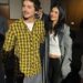 a man in a yellow plaid shirt stands next to a woman in a gray coat and black pants