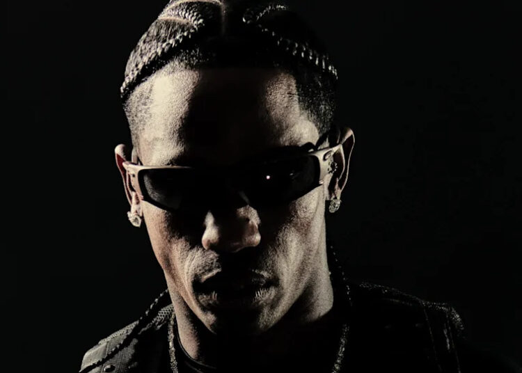 Travis Scott with braided hair and sunglasses, set against a dark background.