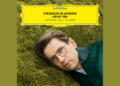 A man with glasses lies on grass, wearing a green coat. The top of the image features a yellow label reading Víkingur Ólafsson Opus 109: Beethoven - Bach - Schubert.