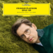A man with glasses lies on grass, wearing a green coat. The top of the image features a yellow label reading Víkingur Ólafsson Opus 109: Beethoven - Bach - Schubert.