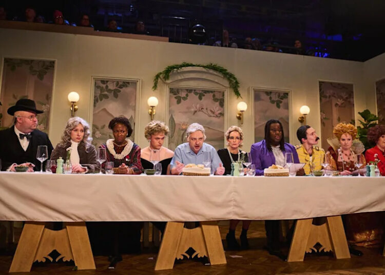 Cast members of Saturday Night Live UK sit at a long table resembling the Last Supper, with an actor playing David Attenborough in the middle, and others including Freddie Mercury and Winston Churchill alongside him