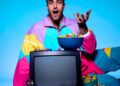 Colorful popcorn surrounds Rob Anderson, sitting on a floor behind a television