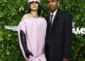 Rihanna in a pink gown with a matching hat and A$AP Rocky in a black suit pose on the green carpet of the Gotham Film Awards.