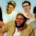A group of five smiling people, each with distinct styles and expressions, against a light blue background.