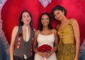 Three people posing in front of a heart-themed backdrop.
