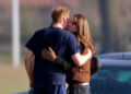 Two people embrace closely beside a parked vehicle in an outdoor area.