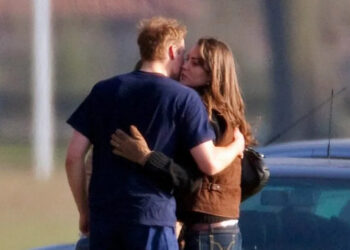 Two people embrace closely beside a parked vehicle in an outdoor area.