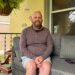 A man sits on a couch on his patio and poses for a photograph.