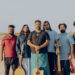 Musical group Raghu Dixit posing in a desert with instruments including a guitar, bass, flute, violin, and mandolin.