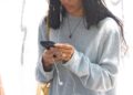 Person wearing a gray sweater and a cap, using a mobile device.