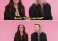 Two people sit against a pink background, smiling. One has long hair and glasses, wearing a dark jacket. The other has shoulder-length hair, also in a dark jacket