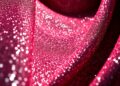 An extreme close-up photograph of a shimmering, sequined fabric texture captured in dramatic high-contrast studio lighting, conceptually representing the glamour and luxury of celebrity red carpet fashion.