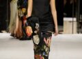 Fashion model wearing an elegant outfit with floral designs, walking on a runway.