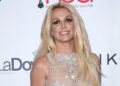 Britney Spears at an event, wearing a sparkly, sleeveless dress with long blonde hair and a smile.