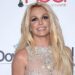 Britney Spears at an event, wearing a sparkly, sleeveless dress with long blonde hair and a smile.
