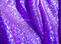 An extreme close-up photograph of shimmering purple sequins and glittering fabric, capturing the glamorous and high-energy atmosphere of a major music festival performance.
